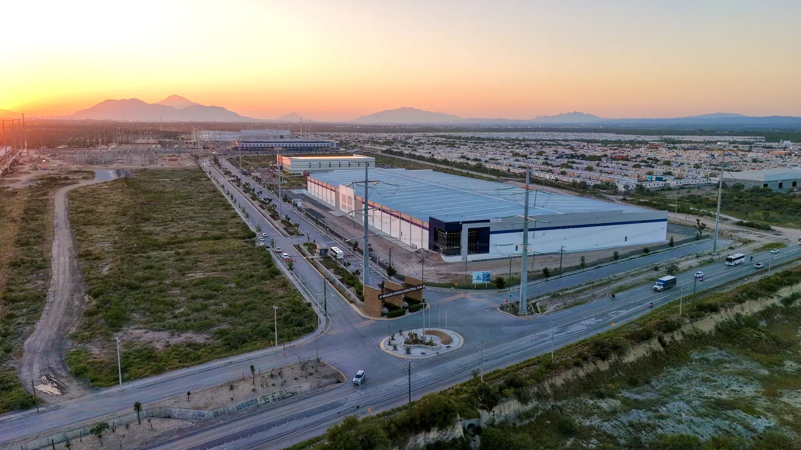 Vista aérea de Mirador Apodaca al atardecer — nave industrial y glorieta de acceso al parque